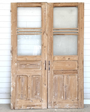 Pair of wooden doors with glass panels against a white wall.