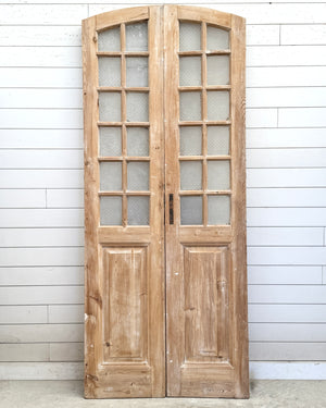 Pair of wooden doors with glass panels against a white paneled wall.