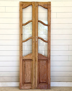 Pair of wooden doors with glass panels against a white paneled wall.
