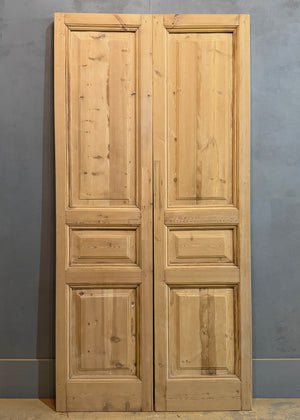 Pair of wooden doors with panel design against a gray wall.
