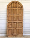 Wooden door with arched top against a white paneled wall