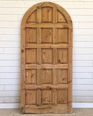 Wooden door with arched top against a white paneled wall