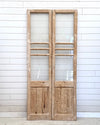 Pair of wooden doors with glass panels against a white paneled wall.