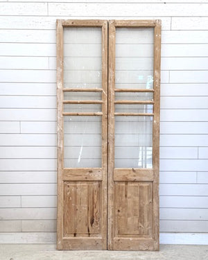 Pair of wooden doors with glass panels against a white paneled wall.